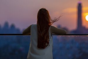 Frau blickt bei Sonnenuntergang von einem Balkon auf die Stadt