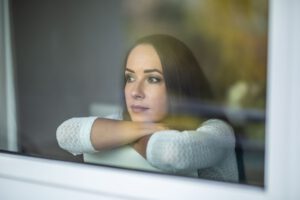 Frau sitzt auf einem Stuhl und blickt nachdenklich durch ein Fenster nach draußen