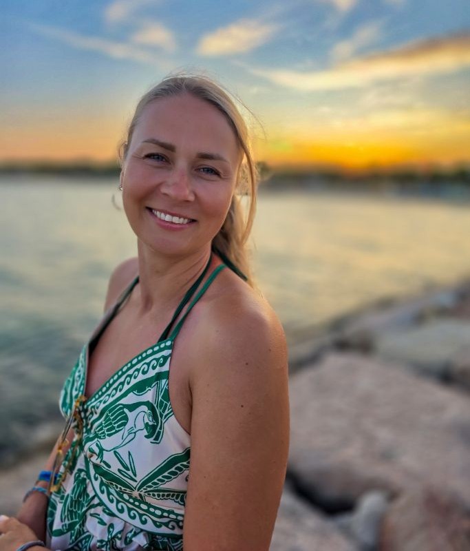Lächelndes Portrait von Maria Koch am Wasser bei Sonnenuntergang – spirituelle Astrologin und Mentorin