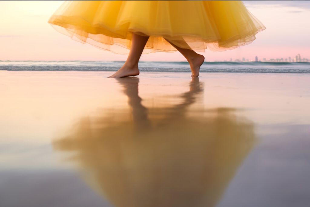 Frau in gelbem Kleid tanzt barfuß am Strand bei Sonnenuntergang – Symbol für Lebensfreude und Selbstsicherheit