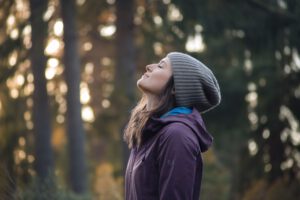 Frau mit grauer Mütze genießt die frische Luft im Wald und blickt achtsam nach oben
