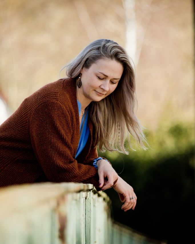 Maria Koch lehnt entspannt an einem Geländer im Freien und wirkt ruhig, nachdenklich und verbunden